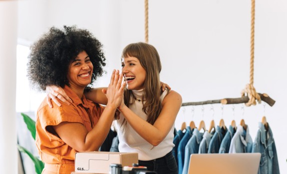Two women giving each other a high-five while preparing packages in a retail store.